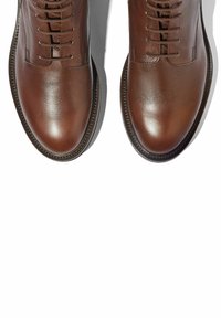 Botas de tobillo de cuero marrón con un acabado suave, que presentan un cierre lateral con cordones y un diseño de punta redonda. Detalles de costura a lo largo de la suela.