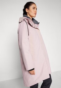 Giubbotto impermeabile rosa chiaro con fodera interna grigia, colletto alto e cappuccio regolabile. Presenta una tasca laterale e una linea dritta elegante.