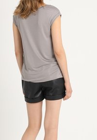 Top corto gris de manga corta hecho de una tela suave, combinado con pantalones cortos de cuero sintético negros con dobladillos enrollados. Vista trasera.