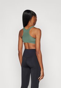 Mørkegrøn atletisk sportstop med racerback-design, parret med høj talje sorte leggings; glat tekstur med minimal branding.
