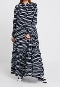 Sukienka z długim rękawem, zapięciem na guziki w granatowym kolorze z białymi owalnymi wzorami. Posiada warstwowy krój i miękki materiał. Noszona z czarnymi sneakersami.