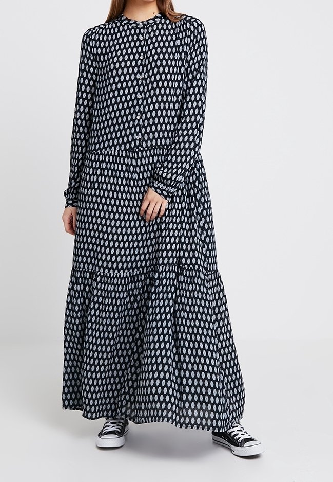 Sukienka z długim rękawem, zapięciem na guziki w granatowym kolorze z białymi owalnymi wzorami. Posiada warstwowy krój i miękki materiał. Noszona z czarnymi sneakersami.
