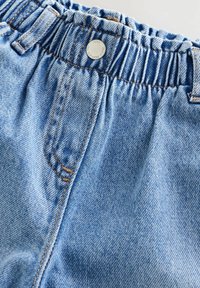 Pantalon en jean bleu clair avec une taille élastique, un bouton en métal et des coutures visibles sur la poche avant.