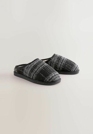 Fekete és szürke kockás papucs, puha gyapjú béléssel, lekerekített orral és fekete gumitalppal; a könnyű felhúzáshoz tervezve.