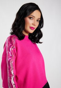 Fuksija pulover s visokim ovratnikom, ukrašen sa sequins detaljima u valovitih uzorcima na rukavima. Mekana tekstura i opušten kroj.