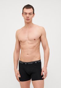 Černé boxerky s měkkým materiálem a elastickým pasem s logem "JACK & JONES". Model je bez trička a stojí vzpřímeně.
