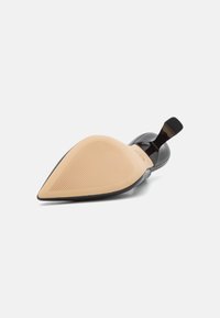 Zapato de tacón alto negro con punta afilada, parte superior de piel sintética brillante y suela de goma beige con líneas de agarre texturizadas.