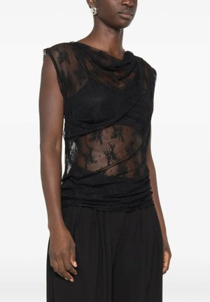 Donna che indossa un top nero in pizzo senza maniche con scollo drappeggiato e motivo floreale trasparente su uno strato nero sottostante.