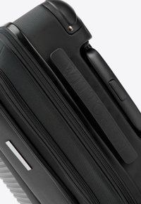 Czarna teksturowana walizka podręczna z wieloma zamkami błyskawicznymi, boczną rączką oraz widocznym logo marki na bocznym panelu.