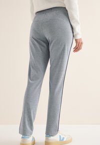 Grijze sportbroek met een gladde textuur, een rechte snit en marineblauwe zijstrepen; gedragen met lichtgekleurde sneakers met blauwe accenten.