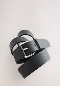 Cintura in pelle nera arrotolata con fibbia rettangolare in argento, appoggiata su uno sfondo chiaro e semplice.