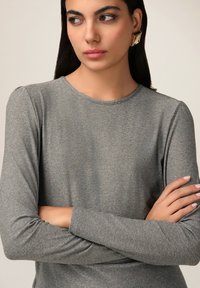 Top gri lung cu mânecă lungă, cu decolteu rotund și textură rasucită. Prezintă mâneci ușor bufante și o siluetă ajustată.