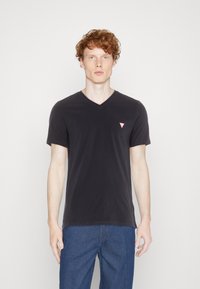 Sort v-hals t-shirt, korte ærmer, blødt bomuldsstof, med et lille rødt trekantet logo på venstre bryst, parret med blå jeans.