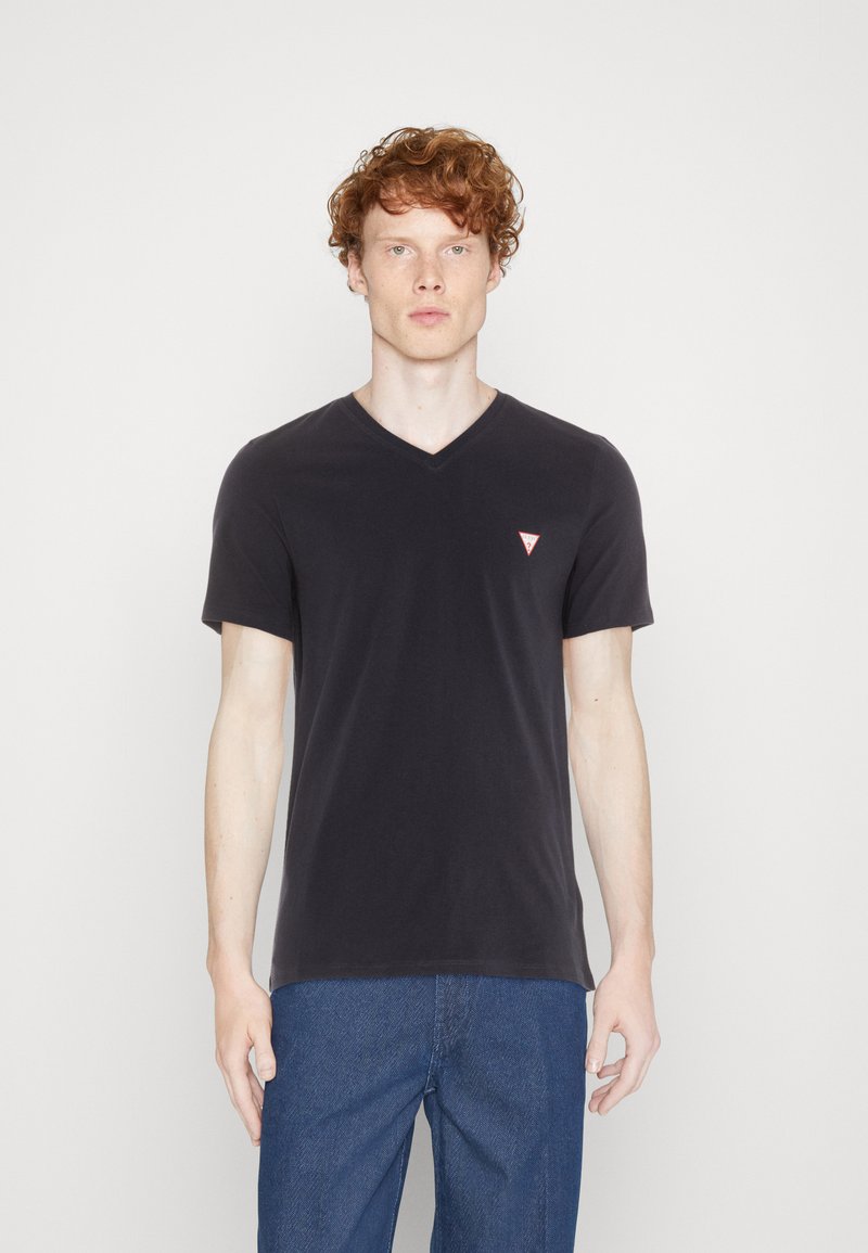 Sort v-hals t-shirt, korte ærmer, blødt bomuldsstof, med et lille rødt trekantet logo på venstre bryst, parret med blå jeans.