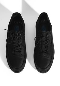 Baskets en cuir noir avec un dessus texturé, un bout rond et des lacets plats. Caractéristiques de textures lisses et granuleuses contrastantes.