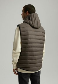 Szary, ocieplany kamizelka z kapturem, z pionowymi szwami, gładką teksturą i luźnym krojem, noszona na jasnoszarym swetrze.