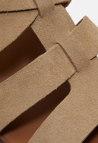 Sangles de sandale en daim beige avec design à découpes et fermeture réglable à scratch.