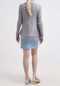 Cardigan grigio a coste con schiena lunga, abbinato a una gonna di jeans azzurro chiaro e scarpe slip-on argentate. Tessuto morbido e design aderente.