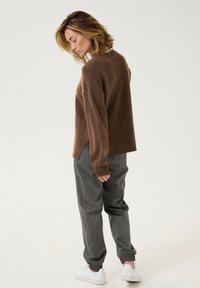 Brun stickad tröja med avslappnad passform, i kombination med grå joggerbyxor. Vita sneakers fulländar outfiten. Enkel, texturerad design.