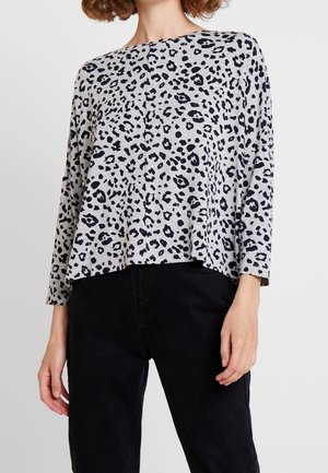 Maglia grigia a maniche lunghe con stampa leopardata nera, vestibilità comoda, scollatura rotonda e orlo inferiore leggermente svasato. Abbinata a pantaloni neri.