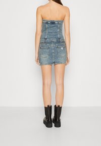 Jeansová mini šaty bez ramínek s přiléhavým korzetem a dvěma zadními kapsami, v světle modrém odstínu s jemným prošíváním. Nosené s černými botami.