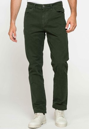 Pantalons en coton vert foncé avec une coupe droite, dotés de cinq poches, d'une fermeture à bouton et d'une texture subtile. Associés à des baskets blanches.
