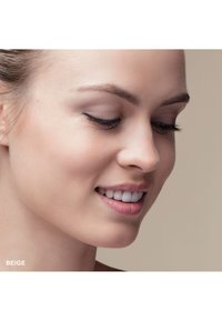 Beige sminkprodukt på en models ansikte, som visar en jämn hudstruktur, ett subtilt leende och välinvuxna ögonbryn mot en neutral bakgrund.