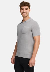 Grau gestreiftes Polohemd mit kurzen Ärmeln, spitzem Kragen, seitlicher Tasche und dezenten Stickdetails, kombiniert mit schwarzen Hosen.