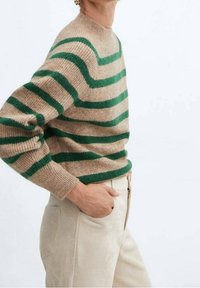 Maglione beige con righe orizzontali verdi, realizzato in un materiale morbido e testurizzato. Presenta un collo alto e una vestibilità rilassata, abbinato a pantaloni chiari.
