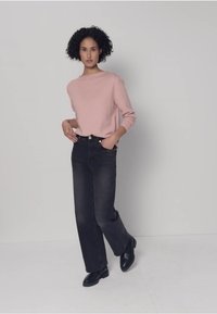 Pull rose clair, jean noir à jambes larges, chaussures noires. Le pull présente un col rond, une coupe décontractée et une texture douce. Le jean a une coupe classique.