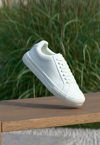 Weißer Sneaker mit einem Obermaterial aus glattem Leder, runder Zehenpartie und traditionellem Schnürverschluss. Verfügt über eine strukturierte Gummisohle und minimalistisches Design.