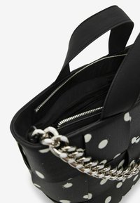 Sac noir à pois blancs, en matériau texturé. Équipé d'une lanière en chaîne argentée et de compartiments zippés à l'intérieur.