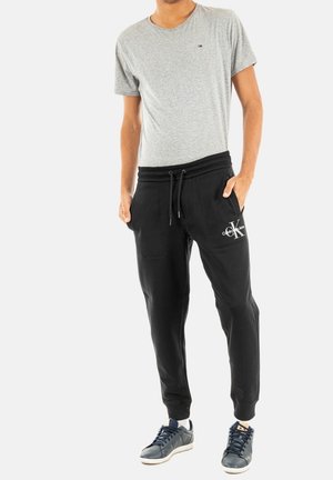 Camiseta gris de manga corta y pantalones jogger negros con cintura elástica y bolsillos laterales; zapatillas deportivas con una combinación de colores azul y blanco.