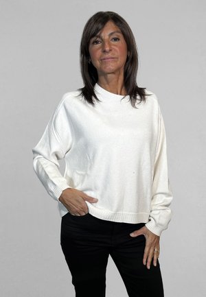Maglione bianco con texture, collo rotondo, spalle scese e polsini a coste, abbinato a pantaloni neri. Design semplice e casual.