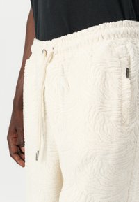 Hvide terry joggers med forhøjet struktureret mønster, elastisk talje, justerbar snor og sidelommer. Blødt stof med en luksuriøs finish.