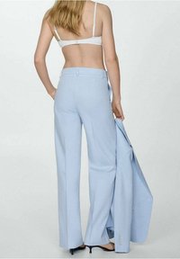Light blue tailored pants with a wide leg, featuring a smooth texture and a high waist. A matching blazer is draped over the arm.