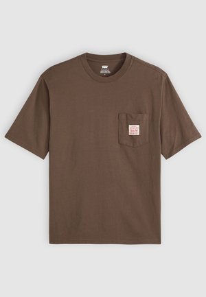 Rjava bombažna majica s kratkimi rokavi, okroglo izrezana, z žepom na levem prsnem delu, ki ima belo etiketo z rdečim besedilom.