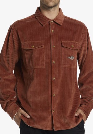 Corduroy shirt in rust orange with vertical ribbed texture, button closures, two chest pockets, and a small logo patch on the left side.