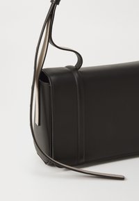 Čierna kožená crossbody taška so štruktúrovaným dizajnom, obsahujúca dlhý ramenný pás a jednoduché, čisté šitie. Hladká textúra s minimalistickým vzhľadom.