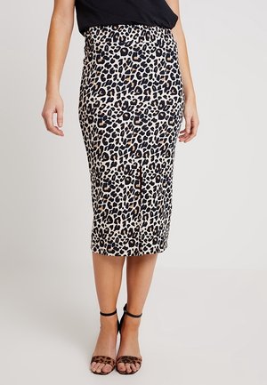 Woman wearing a high-waist, leopard print midi skirt with a front slit, black top, and leopard print ankle-strap heels.