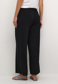 Zwarte wijde broek met een elastische tailleband, gemaakt van een gladde stof. Draagt met blauwe platte sandalen, die een ontspannen ontwerp tonen.