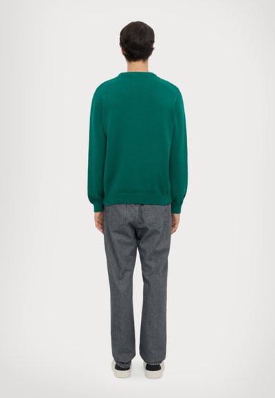 Pull en tricot vert avec encolure ronde, associé à un jean droit gris et des baskets blanches. Le pull a des poignets et un ourlet côtelés.