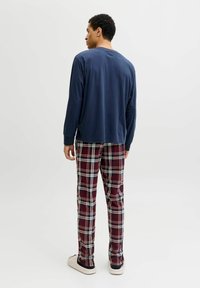 Haut à manches longues bleu marine associé à un pantalon à carreaux rouges avec des accents blancs et bleus. Le pantalon a une coupe décontractée et l'ensemble comprend des chaussures à enfiler.