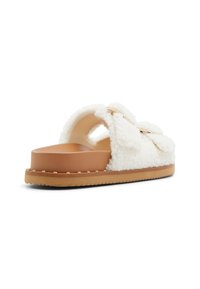 Hvide, fluffy slidesandaler med et rundt slip-on design, tan platformsål og en dekorativ sløjfeaccent. Tekstureret overdel for komfort.