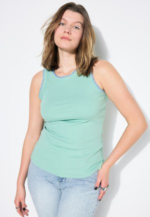 Minzgrünes, geripptes Tanktop mit blauer, gewellter Borte am Ausschnitt und den Armlöchern, kombiniert mit hellblauen Jeans.