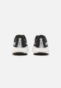 Des chaussures de sport noires avec des semelles blanches et des accents détaillés au niveau du talon. Arborent le nom de la marque sur le côté et possèdent un design lisse et rembourré.