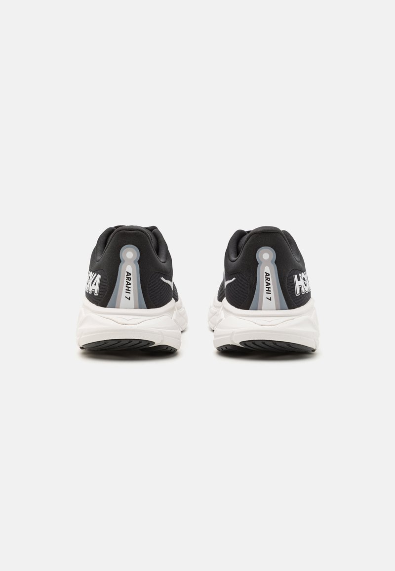 Scarpe da corsa nere con suole bianche e dettagli sul tallone. Presentano il nome del marchio di lato e un design liscio e imbottito.