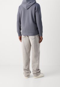 Felpa grigia con tasca a marsupio, abbinata a pantaloni larghi di un grigio chiaro. Sneakers bianche e elementi di design minimal.