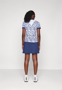 Polo s krátkým rukávem s modro-bílým abstraktním vzorem, doplněný námořnickou sukni. Hladká látka, klasický límec a ležérní design.