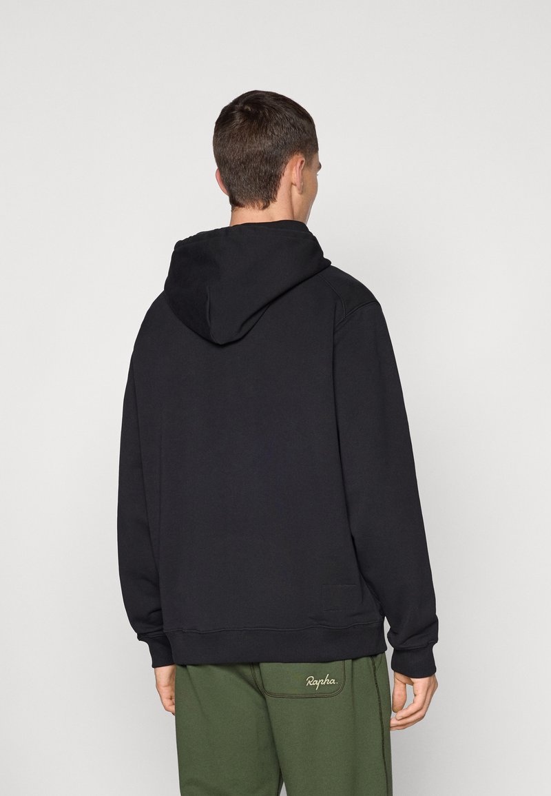 Sort hættebluse med en rummelig hætte, afslappet pasform og ribbede manchetter, parret med olivengrønne træningsbukser med et logo på siden.